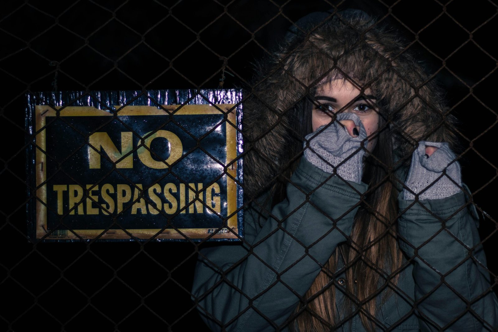A woman in a hooded jacket stands behind a 'No Trespassing' sign, evoking mystery and caution.